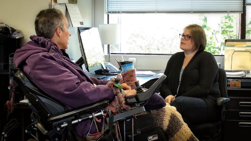 Image of Daphne next to a desk talking with Northwest Access Fund financial coach, Amy.