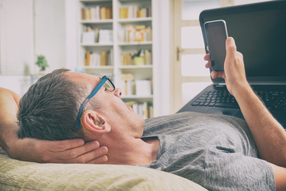 Man using hearing aids laying down looking at his smartphone