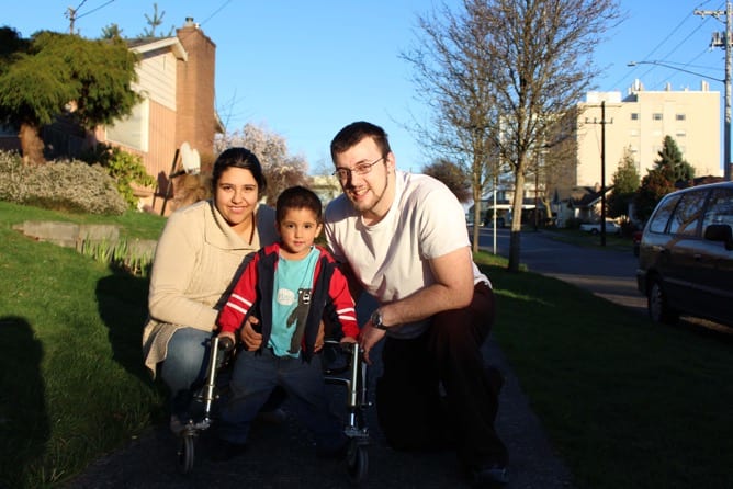 Photo of client family: mom on left, child of about 5 using a walker in the middle, and father on the right