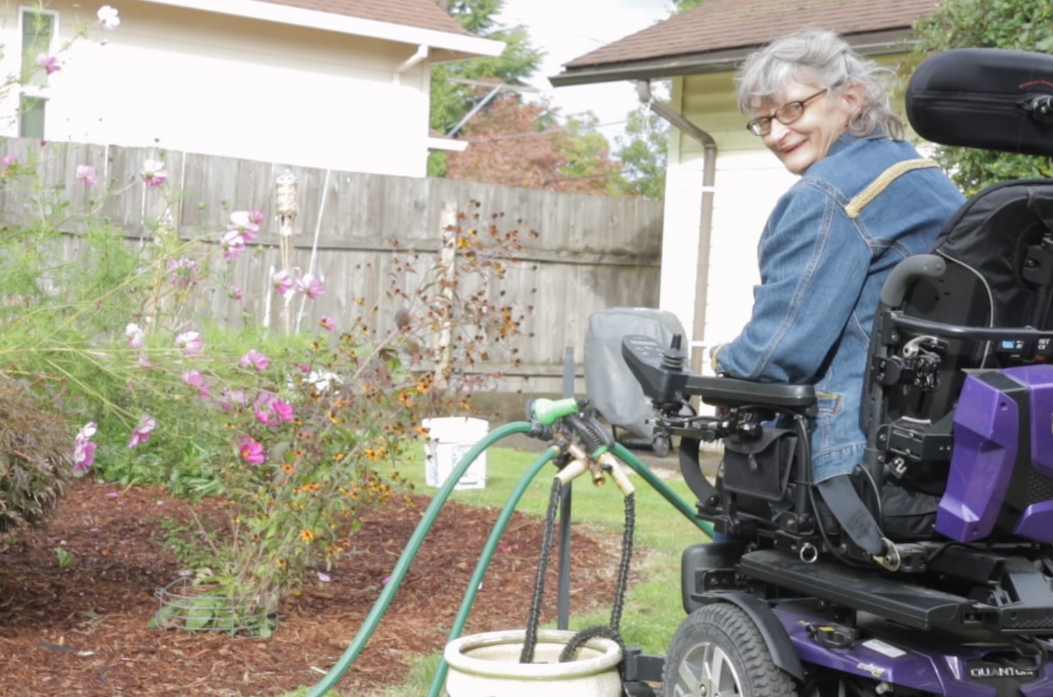 Photo of client who uses a wheelchair in her garden watering her flowers