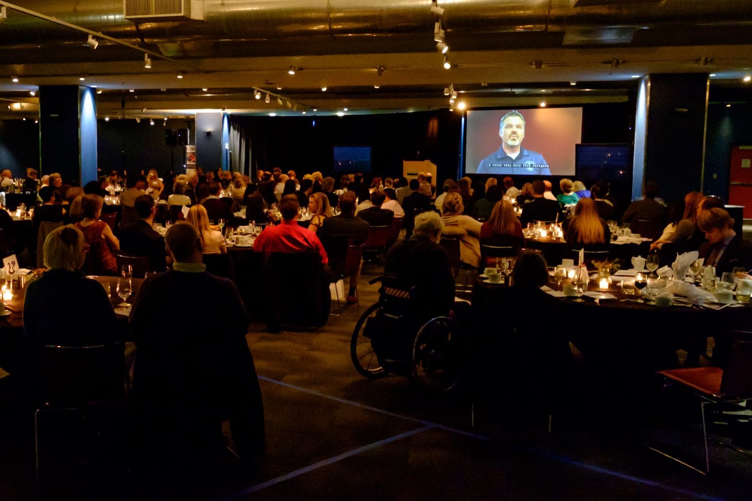 Picture of room during the presentation with tables filled with attendees