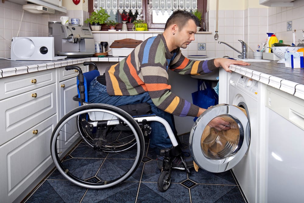 Man using wheelchair putting his laundry in a front loading dishwasher