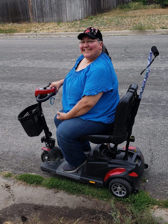 Sandy sitting on her motorized scooter, smiling.