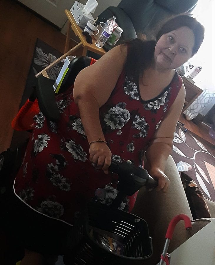 Nancy sitting on her mobility scooter, wearing a red dress with white flowers.