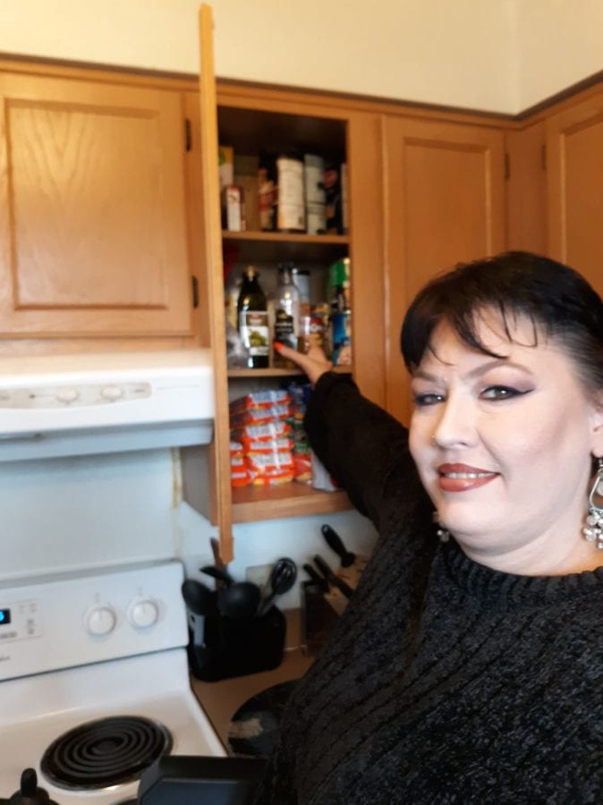 Harley wearing a black sweater, smiling and reaching her cabinet.