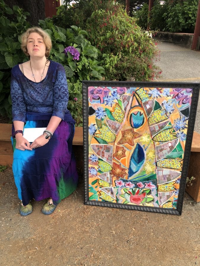 An image of Beth sitting on a wooden bench with a painting she made sitting next to her.