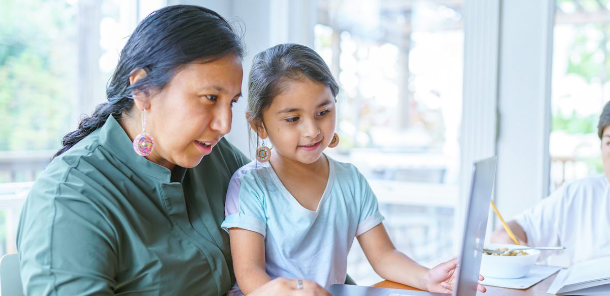 Mom with daughter on lap both looking at laptop on table