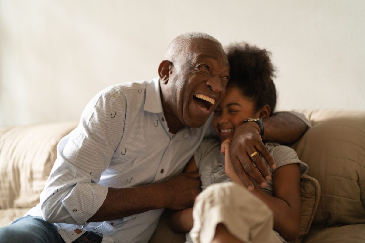 Grandfather laughing and hugging his granddaughter on a beige couch